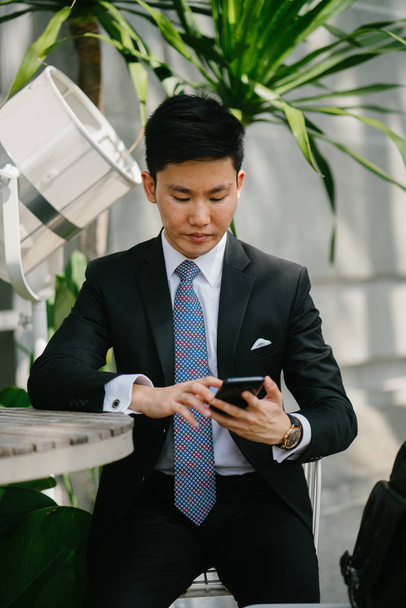 Portrait of a young handsome businessman dressed in a formal suit and tie.. He is is looking down at his smartphone. He looks smart and confident. - Foto, Imagem