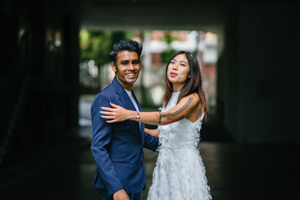  portrait of a young interracial couple getting married. An Indian man and his Chinese wife pose for a photograph in the day along the street against a dark background. - Foto, afbeelding