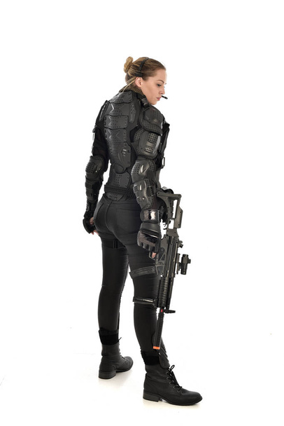 Ganzes Porträt einer Soldatin in schwarzer taktischer Rüstung, die ein Gewehr in der Hand hält, isoliert auf weißem Studiohintergrund. - Foto, Bild