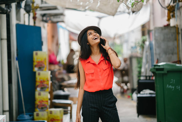divatos és elegáns fiatal indiai ázsiai nő beszél neki a smartphone a nap, egy sikátorban Ázsiában. Ő mosolyogva, és beszél, ő sétál. - Fotó, kép