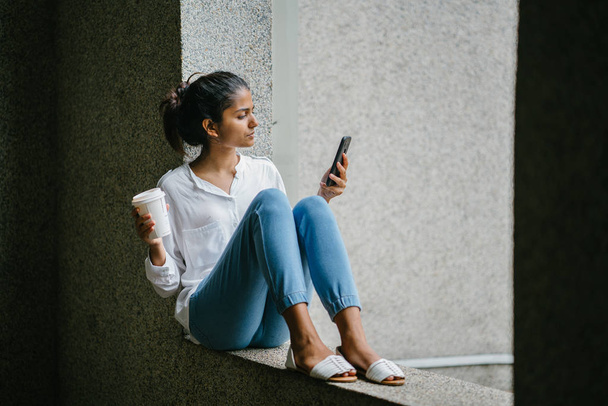 Attractive young Indian Asian woman smiling with a cup of coffee and phone - Foto, afbeelding