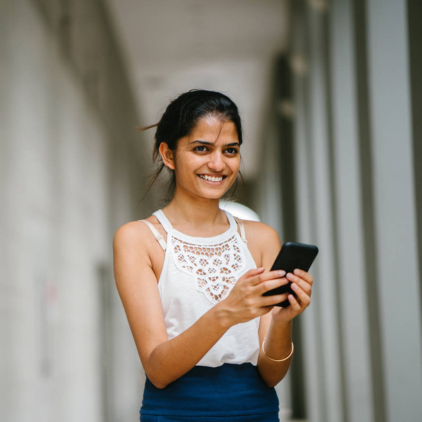 Portrait of attractive and young Indian woman who is dressed professionally. She is standing  with a smartphone - Фото, изображение