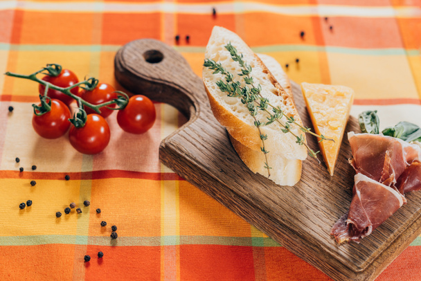 vista superior de baguette en rodajas, carne y queso parmesano en tabla de cortar de madera y tomates cherry frescos en la parte superior de la mesa
 - Foto, Imagen