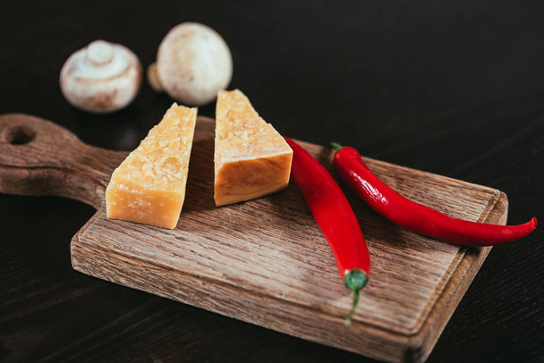 parmesan cheese and chili peppers on wooden cutting board and mushrooms on table - Foto, Imagem