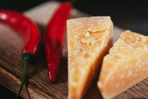 close-up view of gourmet parmesan cheese and chili peppers on wooden cutting board - Фото, изображение