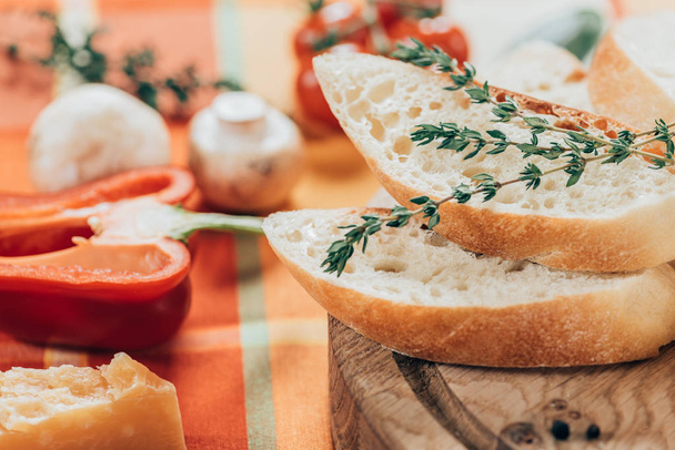 vergrote weergave van vers gesneden stokbrood op houten cutting board en Parmezaanse kaas met paprika en champignons op tafel - Foto, afbeelding