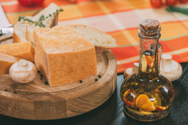 baguette and parmesan cheese on wooden cutting board and oil with spices in glass jug on table - Фото, изображение