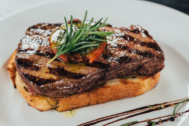 close-up view of delicious juicy beef steak with rosemary and roasted bread on plate  - Photo, Image