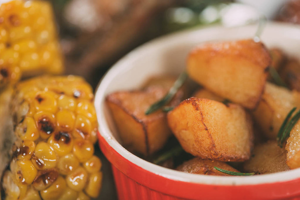 close-up view of tasty grilled corn with roasted potatoes on plate - Foto, afbeelding