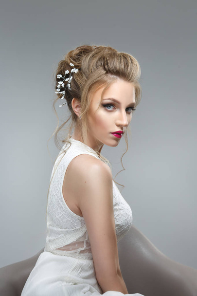 Elegant bride with a beautiful hairstyle and bright make-up on a gray background. - Фото, зображення