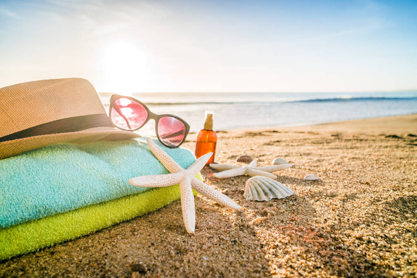 Zonnebril, handdoeken, hoed, zonnebrandcrème, schelpen en zeesterren op sandy - Foto, afbeelding