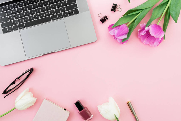 Office desk with laptop, white tulips, glasses, pen and scissors on pink background. Flat lay. Top view. Freelancer composition with copy space. - 写真・画像