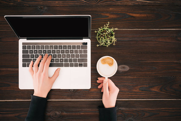 Vista recortada de las manos de la mujer en el ordenador portátil con pantalla en blanco y taza de café
 - Foto, Imagen