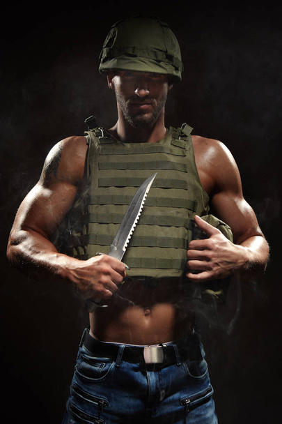 Muscle hero man in tactical vest and helmet armed with survival knife - Foto, imagen