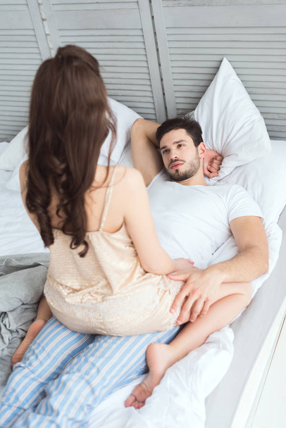 partial view of young man looking at girlfriend in pajamas on bed - Фото, изображение