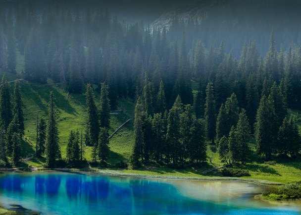 Místico lago de aspecto azul profundo con bosque de coníferas en sus orillas y niebla por encima de ella - Foto, Imagen