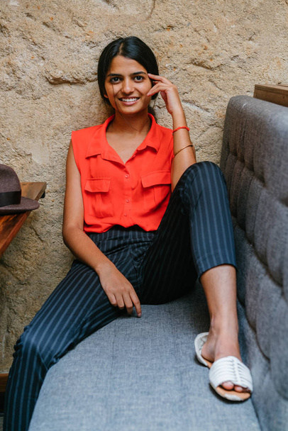 Portrait of a young and attractive Indian Asian woman smiling at the camera. She is seated and has a brown fedora cap . She is dressed in smart casual and is relaxed and cheerful. - Zdjęcie, obraz