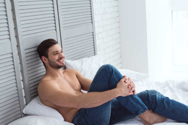 mladý atraktivní muž v džínách, ležící na posteli - Fotografie, Obrázek
