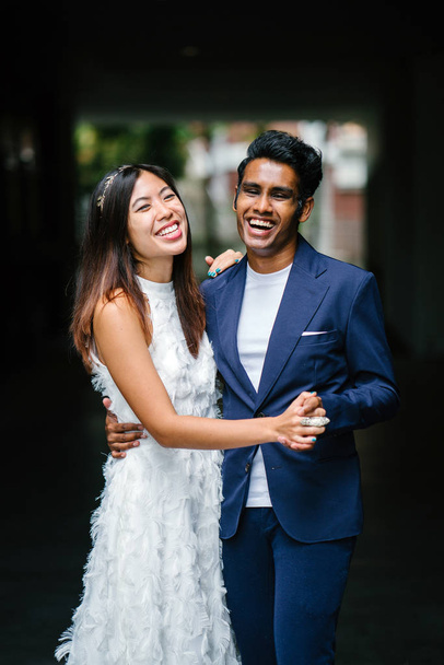  portrait of a young interracial couple getting married. An Indian man and his Chinese wife pose for a photograph in the day along the street against a dark background. - Fotó, kép