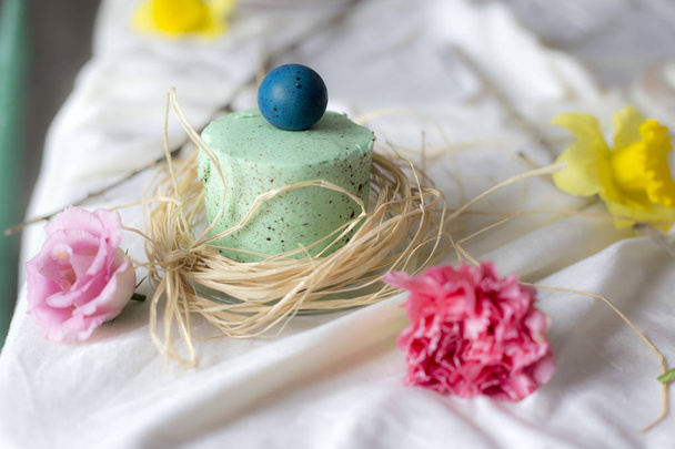 Easter mini cake with painted egg wrapped in dry grass, blurred holiday table background - Photo, image