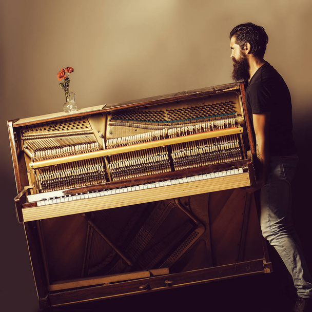 bearded man trying to move wooden piano with rose - Φωτογραφία, εικόνα