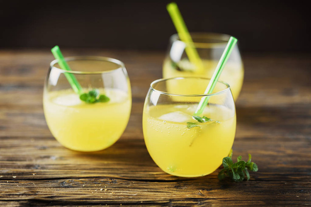 Glasses of orange cocktails with ice and mint, wooden table - Photo, Image