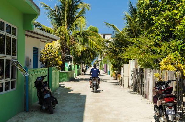 Huraa, Maldives - November 20, 2017: The central street of the Huraa island with one-story houses and tall palm trees overlooking the Indian Ocean, Kaafu Atoll, Kuda Huraa Island, Maldives - Фото, изображение