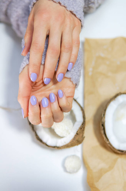 Stylish trendy female manicure with coconut on the background. Beautiful young woman hands with purple gel polish - Fotó, kép