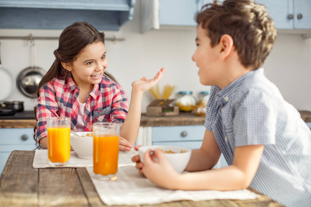 Cheerful girl talking with her brother at breakfast - Foto, afbeelding