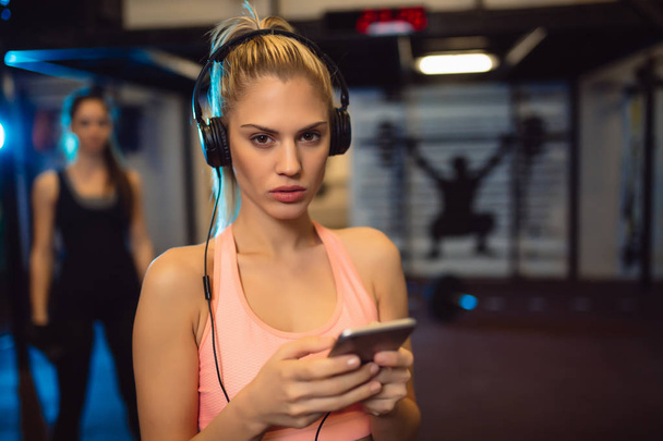 Gros plan de la jeune sportive avec smartphone écoutant de la musique en salle de gym
. - Photo, image
