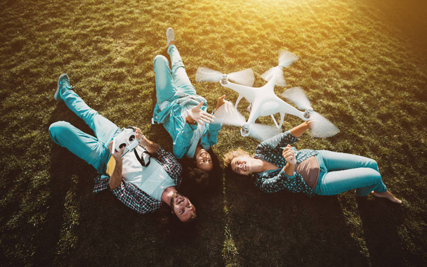 Gesellschaft von drei Personen im Gras und fliegender Drohne - Foto, Bild