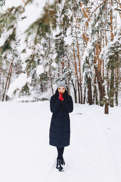 The girl walks in a snow-covered forest among the pines in red g - 写真・画像