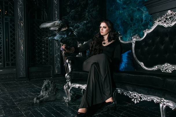 young beautiful caucasian woman with black raven on her hand sitting on sofa - Foto, Imagem