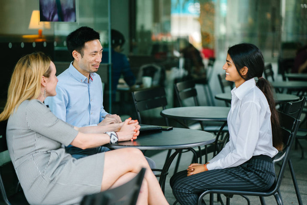 young Indian Asian woman is interviewing for a job and is speaking with a diverse interview panel in an office in the day. One interviewer is a Chinese man and the other a caucasian woman. - 写真・画像
