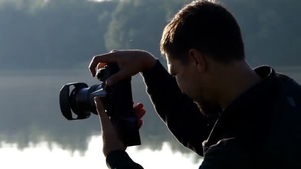 Молодий чоловік стріляє гарним озером зі своєю камерою на заході сонця
 - Кадри, відео