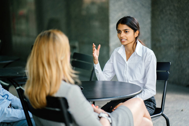  young and attractive Indian Asian woman is interviewing for a job. She is dressed professionally in a white shirt and is sitting and talking to her interviewers. She is confident and relaxed. - Photo, image