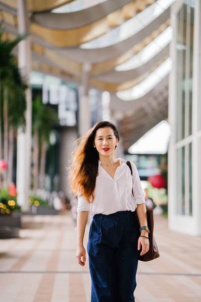 Portrait of a young Singaporean Chinese Asian woman executive walking outdoors in the city. She is smartly and elegantly dressed in corporate wear and is walking. - Фото, зображення
