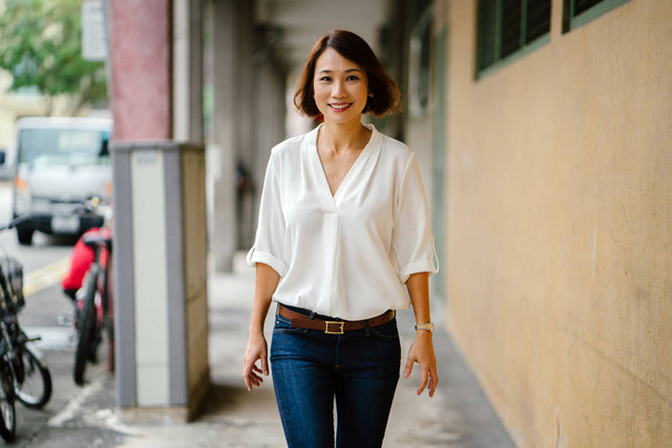  young Chinese Asian woman walks along a corridor in Singapore, Asia. She is dressed smartly in business casual, has bobbed hair and is smiling as she strolls down the corridor. - Foto, immagini