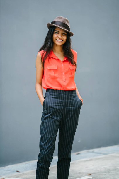 Portrait of a young, attractive Indian Asian fashion student. She is smiling and standing in the sun against a plain grey blue background. - Fotografie, Obrázek