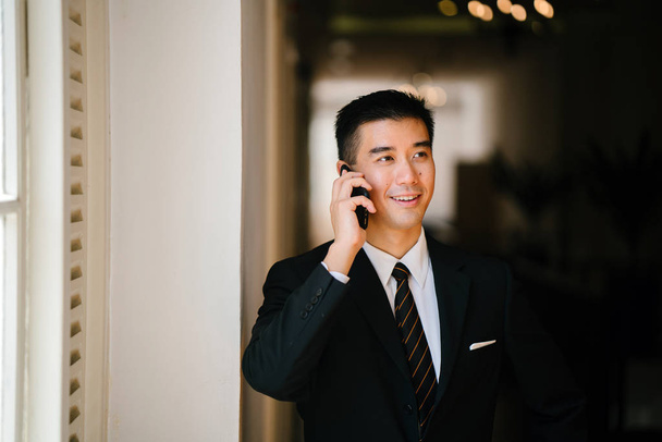 Portrait of young and handsome Chinese Asian man in a suit with his smartphone. - Valokuva, kuva