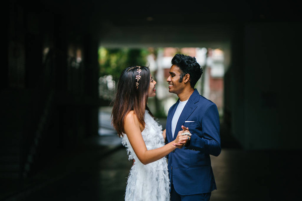  portrait of a young interracial couple getting married. An Indian man and his Chinese wife pose for a photograph in the day along the street against a dark background. - 写真・画像