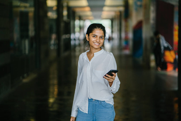 Portrait of attractive and young Indian woman who is dressed professionally. She is standing  with a smartphone - Foto, Bild