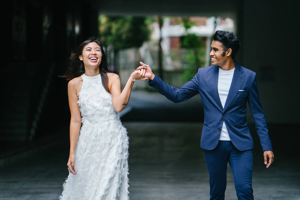  portrait of a young interracial couple getting married. An Indian man and his Chinese wife pose for a photograph in the day along the street against a dark background. - Photo, image