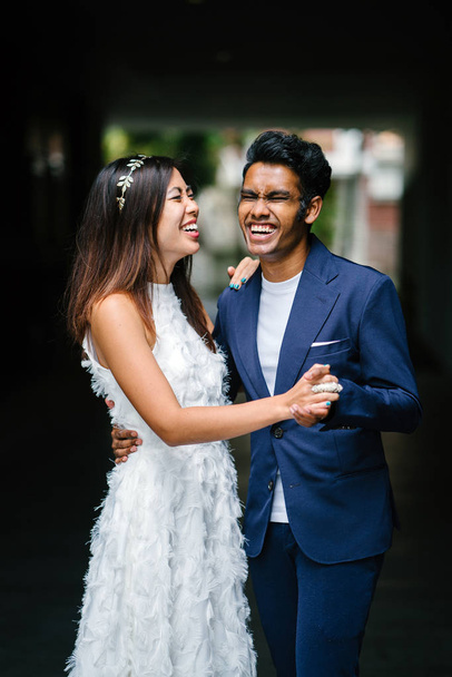  portrait of a young interracial couple getting married. An Indian man and his Chinese wife pose for a photograph in the day along the street against a dark background. - Фото, зображення