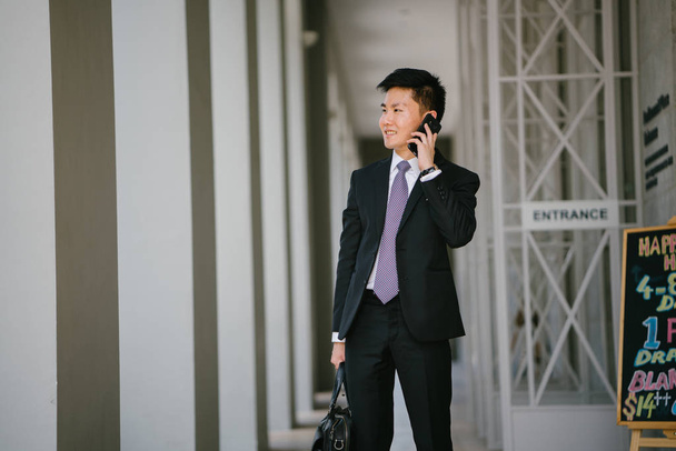 Portrait of a young handsome businessman dressed in a formal suit and tie.. He is is looking down at his smartphone. He looks smart and confident. - Fotografie, Obrázek