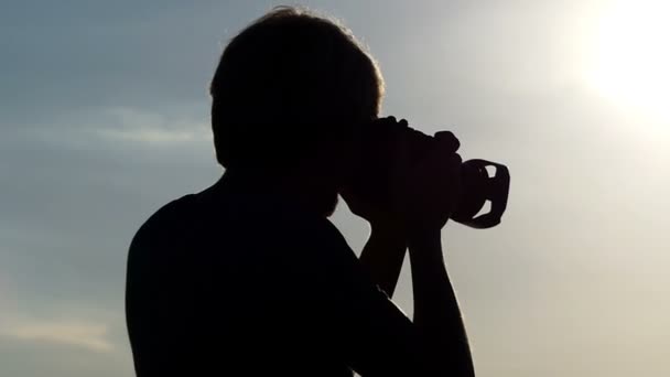 Νεαρός άνδρας στέκεται σε ένα δάσος στη λίμνη και εξετάζει τη φωτογραφική μηχανή του το καλοκαίρι - Πλάνα, βίντεο