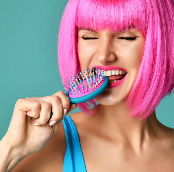 Closeup portrait of happy fashion brunette woman close mouth with colorful pink blue yellow small hair comb brush in pink wig - Foto, immagini