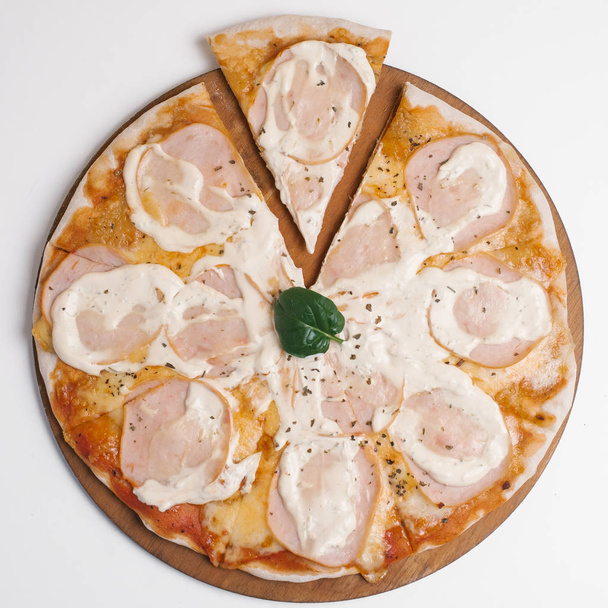 Pizza mit Tomatensauce, Sahnesauce, Mozzarella und Schinkenscheiben dekoriert mit Spinatblatt serviert auf hölzernem Pizzateller - Foto, Bild