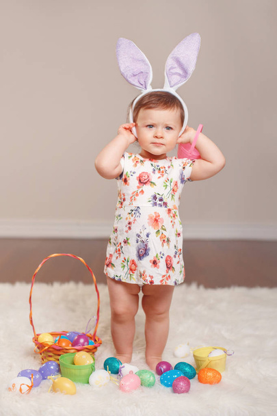 Cute adorable Caucasian baby girl wearing Easter bunny rabbit ears playing in studio indoors. Kid holding basket with eggs celebrating traditional holy Christian holiday - Photo, Image