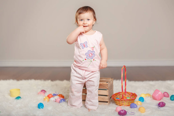 Cute adorable Caucasian baby girl in pink shirt and pants celebrating traditional Easter Christian holiday. Kid child holding basket and playing with colorful eggs - Photo, Image